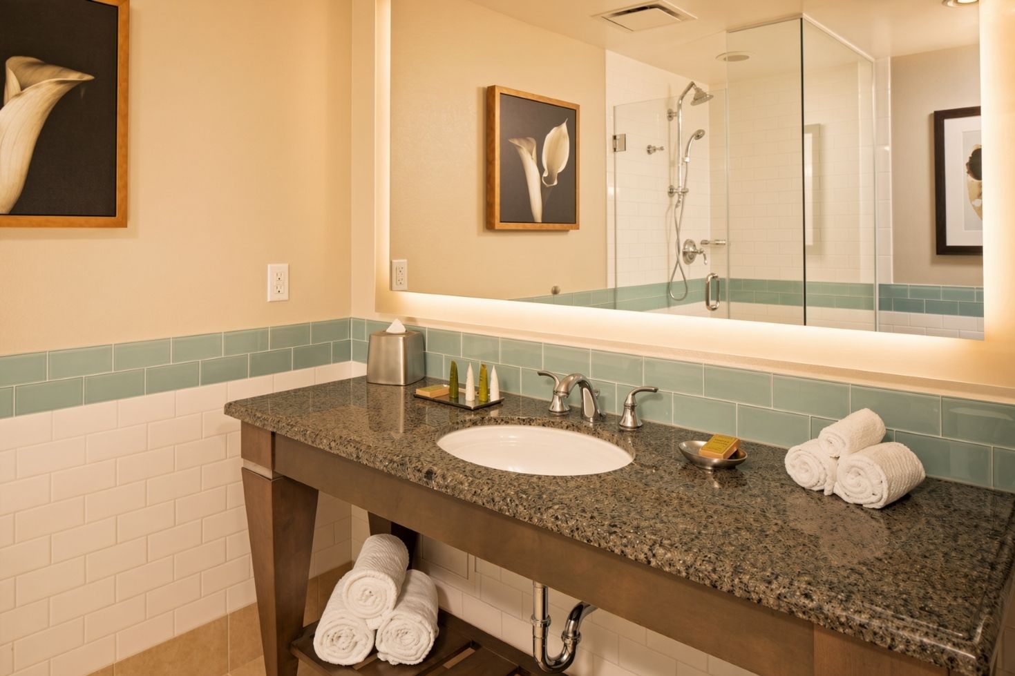 A bathroom with a granite countertop, a white sink, a mirror, a towel rack, and a shower area.
