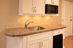 A kitchen with a granite countertop, stainless steel sink, white cabinetry, a black microwave, and a dishwasher. - Orlando | Quick Disney Retreat | Pool + Parks (Orlando)