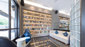 A modern lobby with a large bookshelf, a white sofa with blue pillows, and a black leather chair.