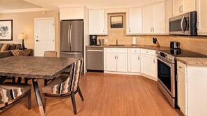 A modern kitchen with white cabinets, stainless steel appliances, a granite countertop, and a dining area with a dark table and patterned chairs. - Orlando | Romantic Park Retreat | Pool + Parks (Orlando)