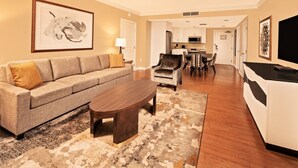 A living room with a sofa, coffee table, and a TV. There is a dining area with chairs and a table. The room has wooden flooring and a patterned rug. - Orlando | Upscale Disney Retreat | Pool + Parks (Orlando)