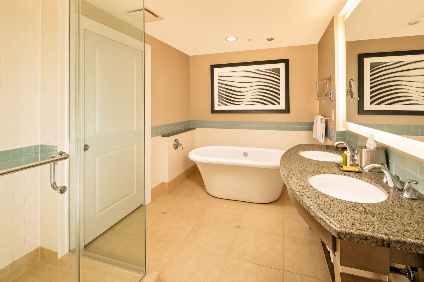 A bathroom with a glass shower door, a freestanding bathtub, and two sinks with granite countertops.