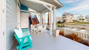 A covered outdoor area with a table and chairs, a wooden staircase, and a view of the beach and other buildings. - Resort Pools, Golf Cart Boardwalk to Beach (Port Aransas)