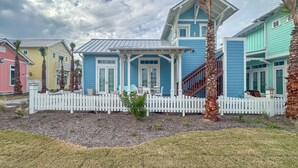 A row of colorful houses with a white picket fence, a small garden, and a cloudy sky. - Resort Pools, Golf Cart Boardwalk to Beach (Port Aransas)
