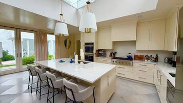A modern kitchen with a large island, bar stools, and a view of the outdoors through large windows.