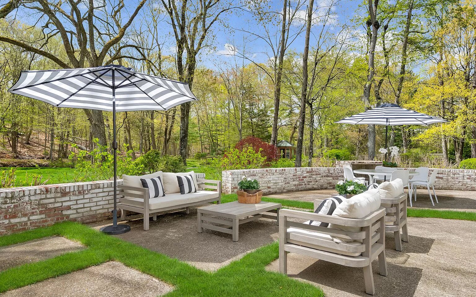 Un espace extérieur aménagé en terrasse, avec un mur en briques, un banc en bois, une table et deux parasols à rayures.