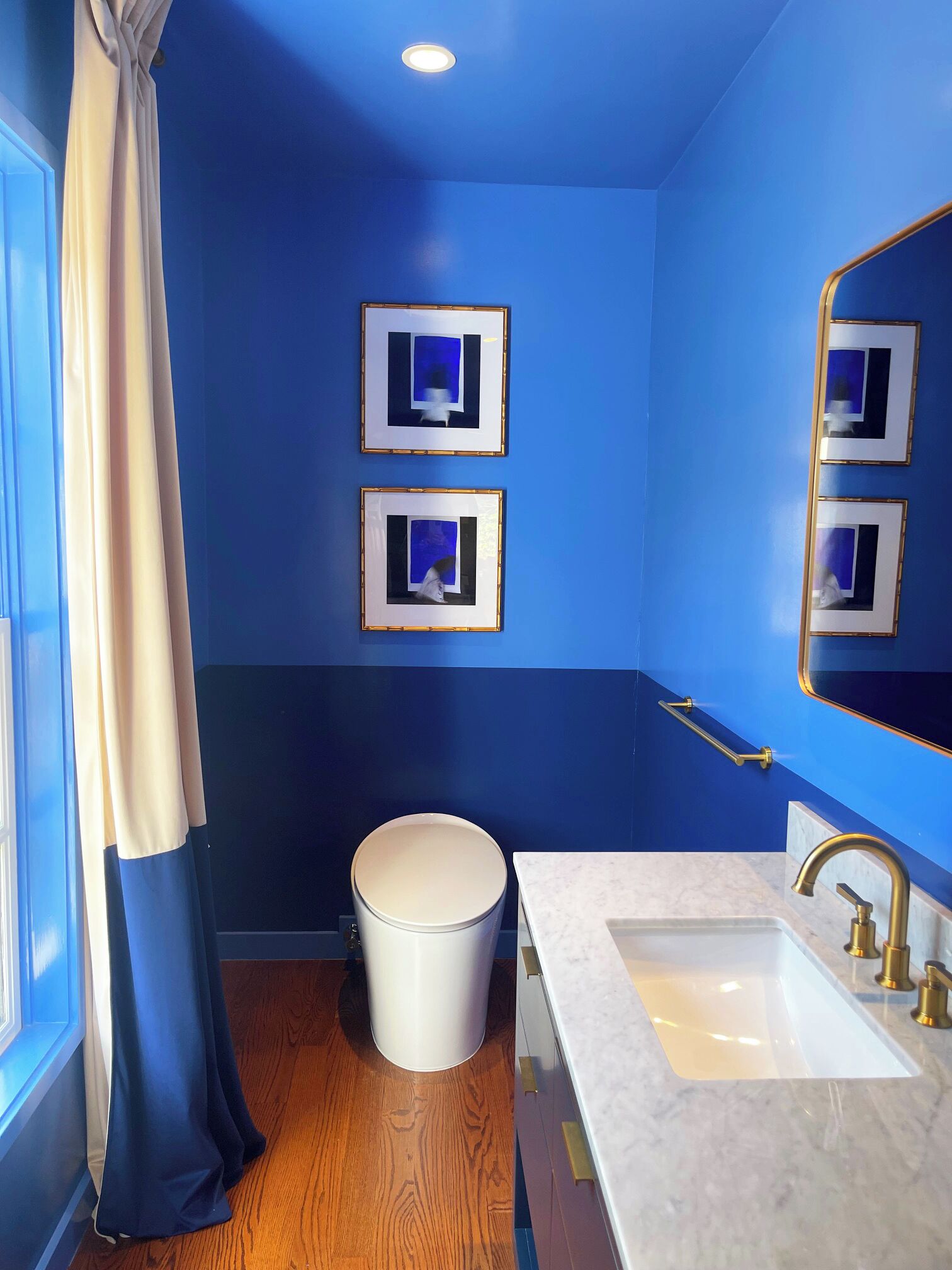 Un baño con paredes azules, un inodoro blanco, un lavabo con grifo dorado y cuadros en la pared.