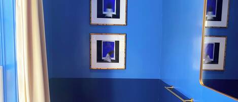 Un baño con paredes azules, un inodoro blanco, un lavabo con grifo dorado y cuadros en la pared.