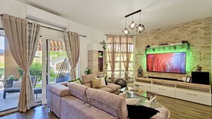 Een moderne woonkamer met een grote flatscreen televisie, een bank, een salontafel en een wand met een stenen textuur.