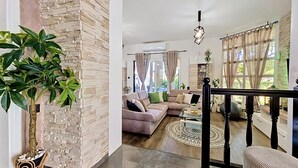 Een moderne woonkamer met een accentmuur van steen, een grote plant, een zithoek en een eethoek met een kamerbreed tapijt.