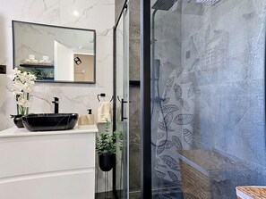 Une salle de bain moderne avec un lavabo en marbre, un receveur noir, un miroir, une cabine de douche en verre et une plante en pot.