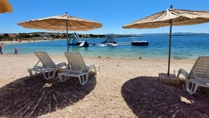 Een strand met ligbedden en parasols, een heldere blauwe zee en boten op het water.
