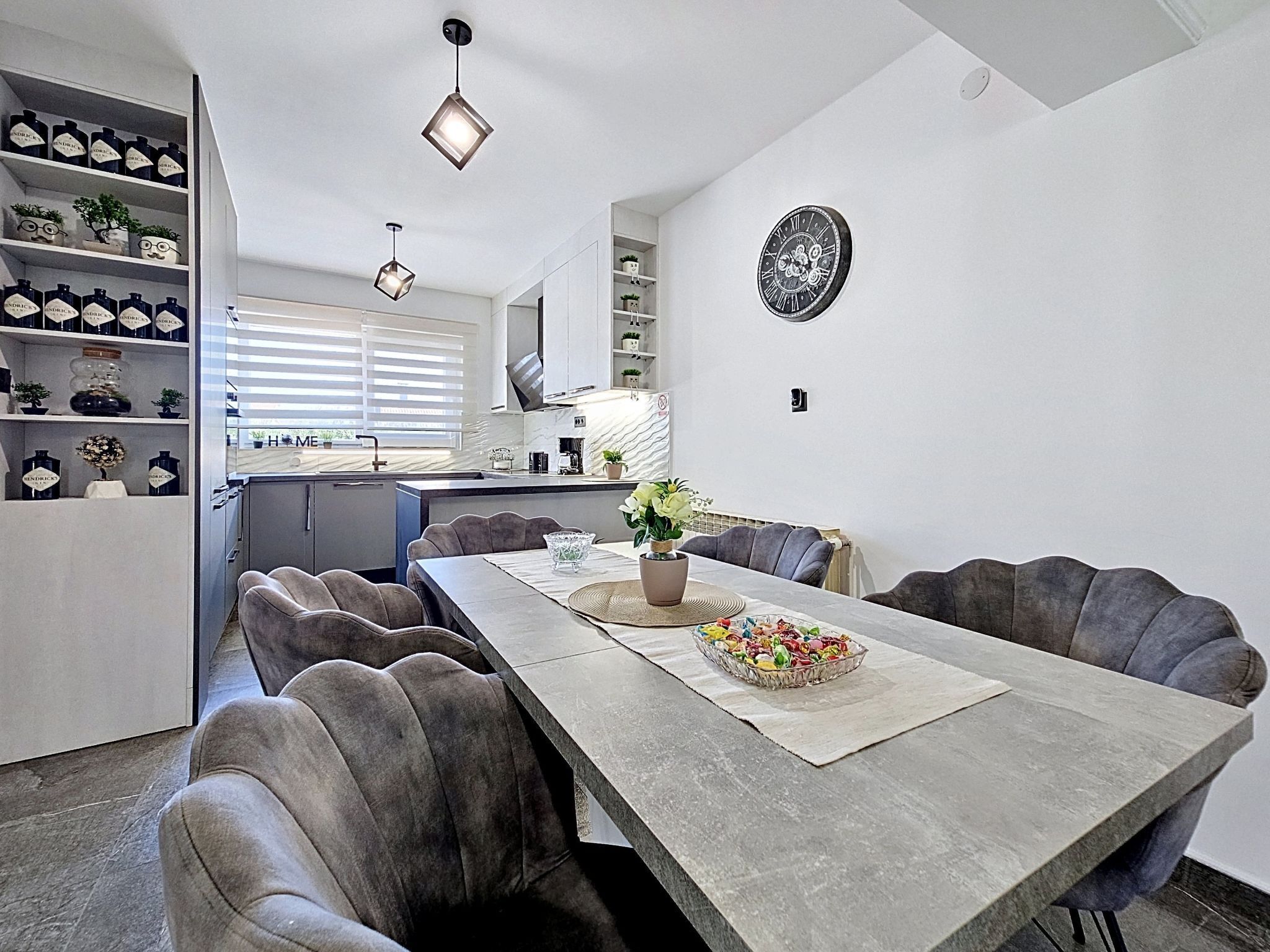 A modern kitchen with white cabinets, a dining table with chairs, and a clock on the wall.