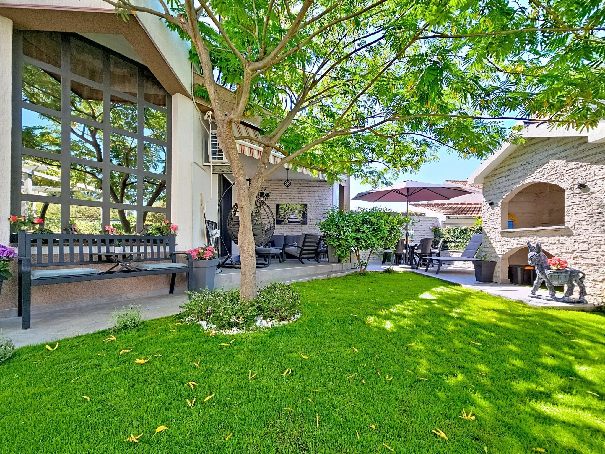 A courtyard with a stone wall, a tree, a bench, outdoor seating, and a statue.