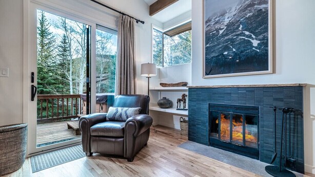 A modern living room with a fireplace, a leather chair, and a large window overlooking a deck.