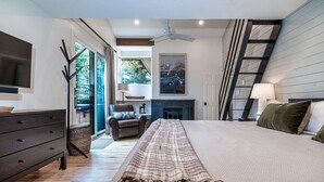 A modern bedroom with a large bed, a flat-screen TV, a fireplace, a ladder, and a view of the outdoors.
