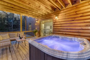 Une cabane en bois dotée d’un bain à remous, d’une terrasse en bois et d’une porte vitrée donnant sur la cuisine.