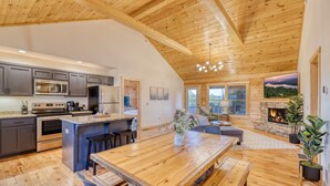 A spacious kitchen with modern appliances, a large wooden dining table, and a cozy fireplace area. - Ellijay Escape: Hot Tub, Fireplace, Peaceful Views (Ellijay)