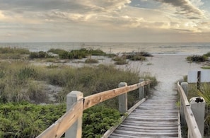 A wooden boardwalk leading to a beach with overcast skies.