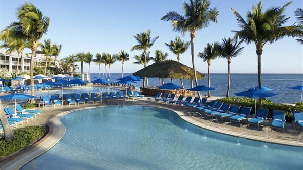 A poolside area with lounge chairs and umbrellas, surrounded by palm trees and a view of the ocean.