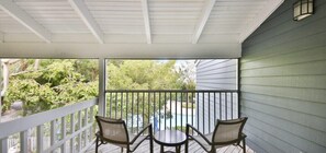 A covered porch with a railing, two chairs, and a small table.