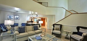 A spacious living area with a sofa, armchairs, and a coffee table. A staircase with a geometric railing leads to an upper level.