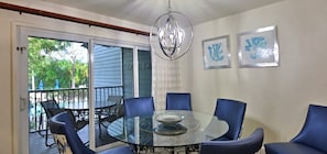 Zona pranzo con tavolo in vetro circondato da sedie blu, un lampadario e opere d'arte alle pareti.