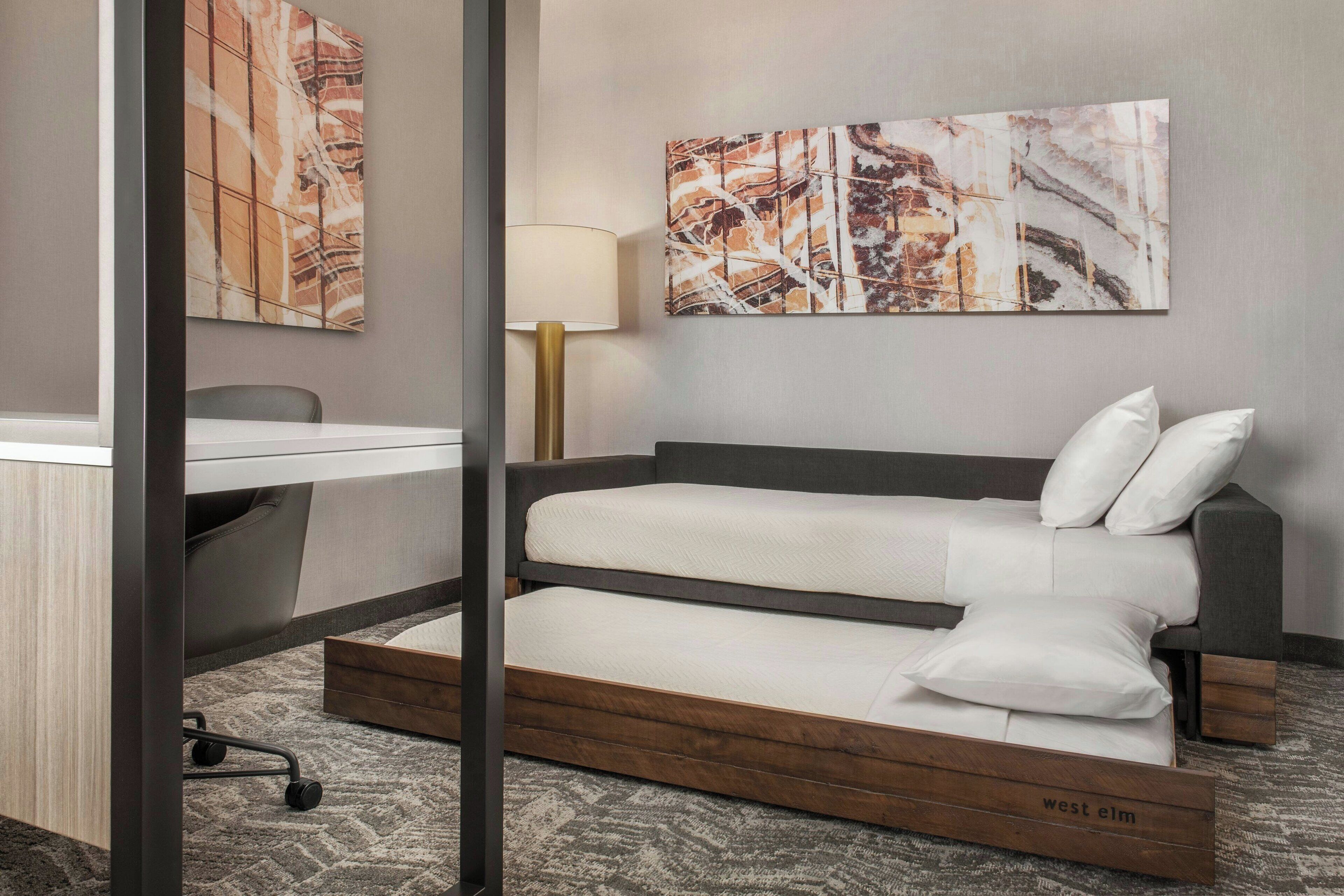 A hotel room with a bed, a desk, and two large abstract paintings on the wall.