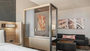 Una habitación de hotel moderna con cama, escritorio con espejo, sofá y obras de arte en las paredes.