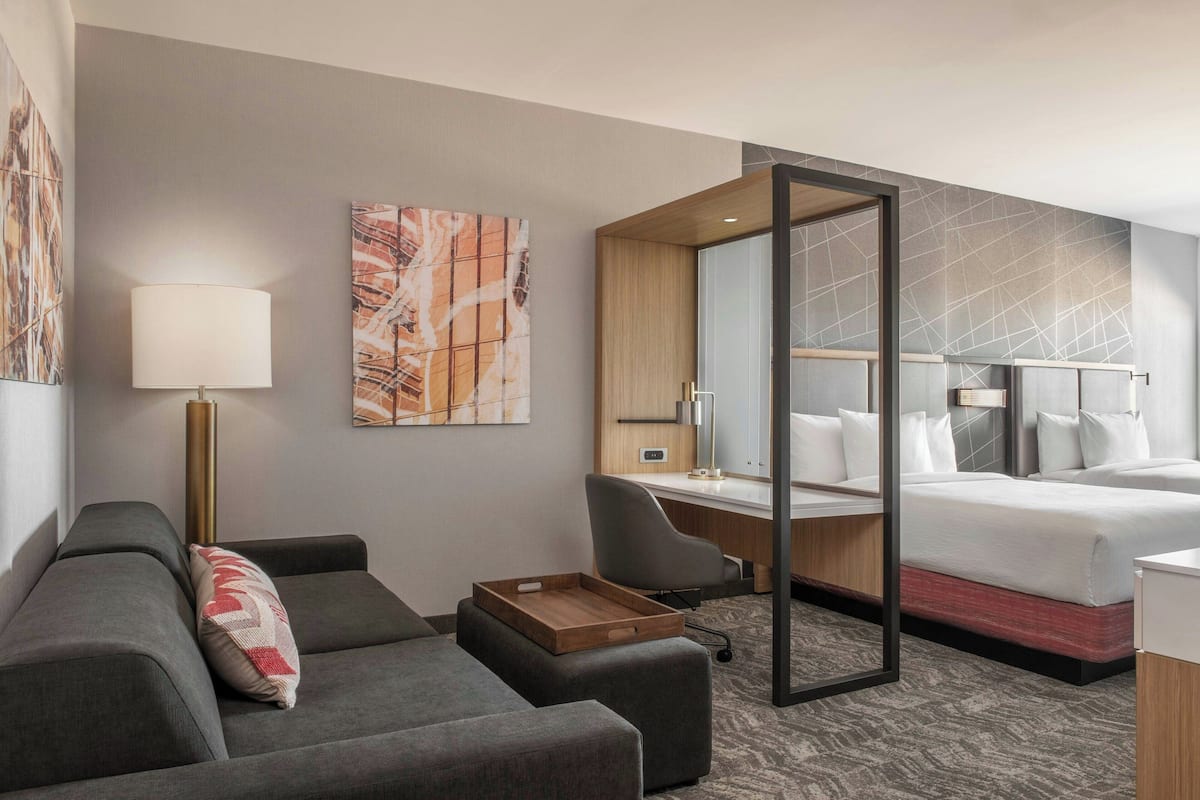 A modern hotel room with a sofa, a desk, a bed, and a large mirror.