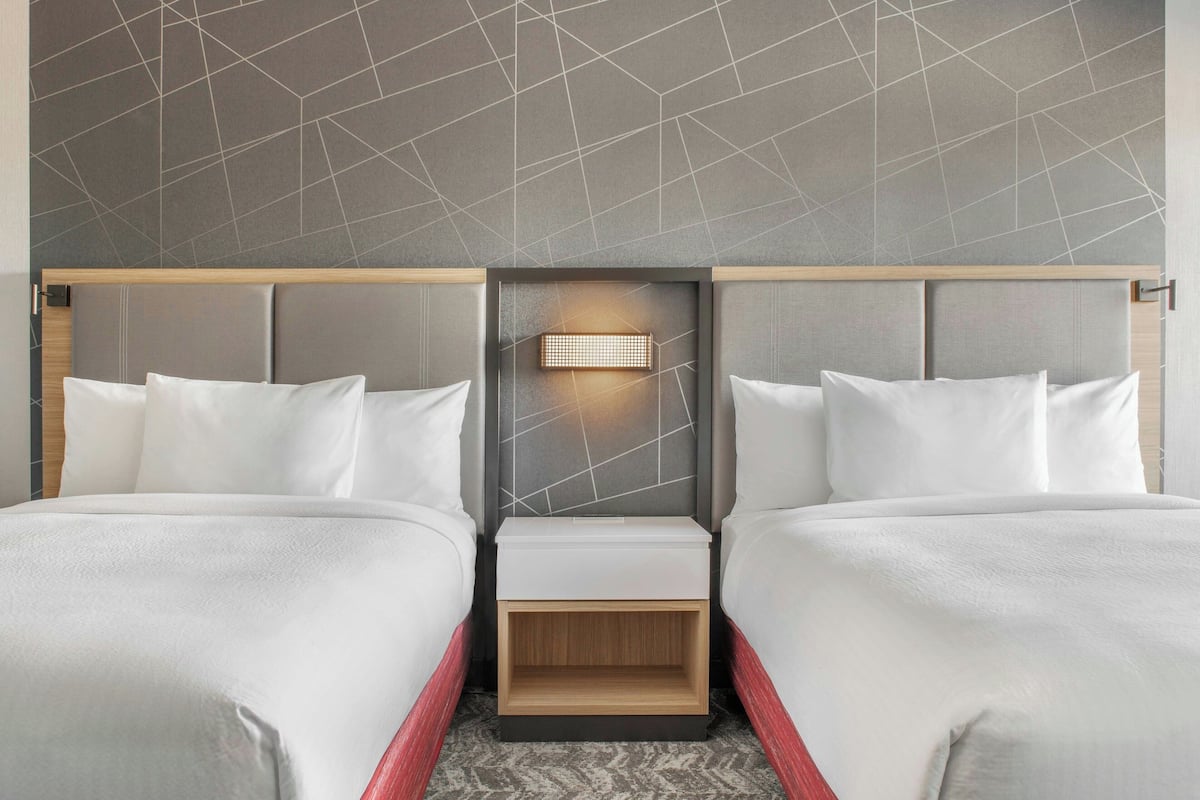 A hotel room with two beds, a nightstand with a light, and a geometric-patterned wall.