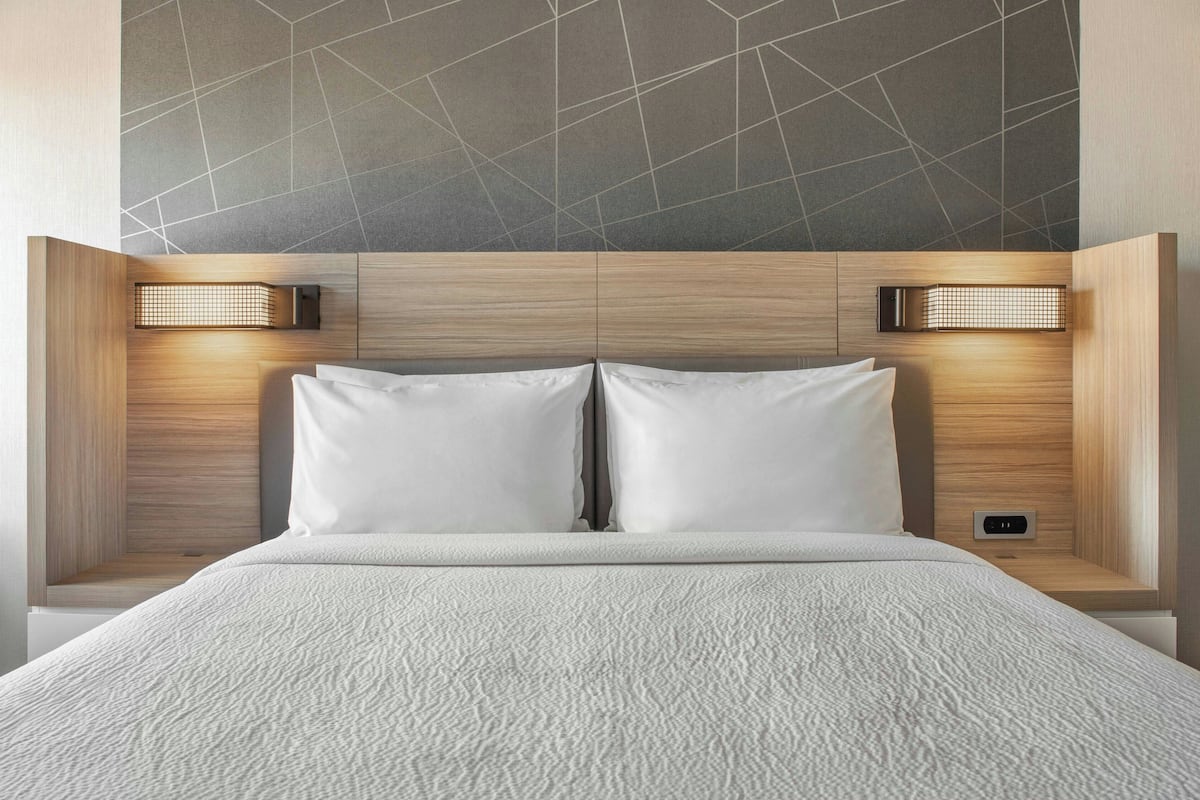 A modern hotel room with a large bed, wooden headboard, and two wall-mounted reading lights.