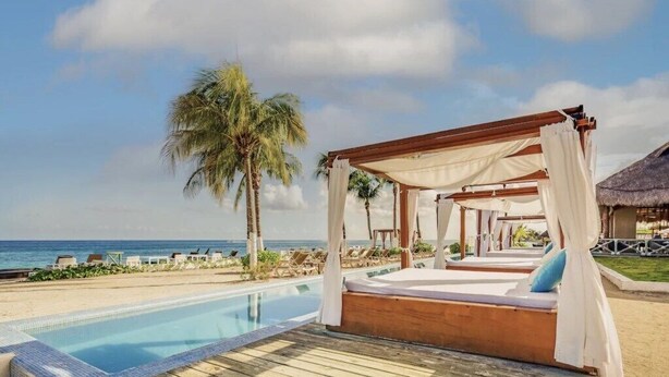 Un resort frente al mar con muelle de madera, piscina y cama con dosel con vista al océano.