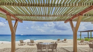 Un patio frente a la playa con un toldo a rayas, sillas de playa y una mesa.