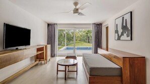 Una sala moderna con televisor de pantalla plana, muebles de madera, ventilador de techo y vista a una piscina.