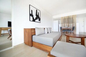 Ein modernes Wohnzimmer mit grauem Sofa, einer Wand in Holzoptik, einem runden Holztisch und einem Essbereich mit Stühlen und Tisch.