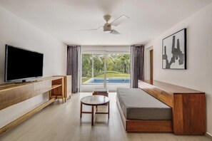 A modern living room with a flat-screen TV, wooden furniture, a ceiling fan, and a view of a swimming pool. - Cozumel | Couples All-Inclusive Getaway | Pool + Beach (Cancun)