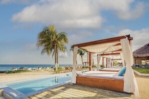 Ein Strandresort mit Holzterrasse, Pool und einem Himmelbett mit Blick auf den Ozean.