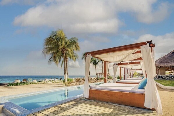 Un resort frente al mar con muelle de madera, piscina y cama con dosel con vista al océano.