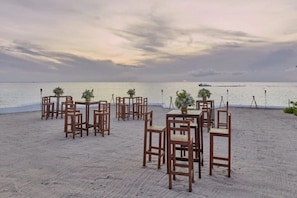 Un espace de restauration aménagé sur la plage, avec des tables et des chaises en bois, préparé pour un repas en plein air.