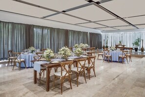Ein geräumiger Festsaal mit mehreren runden Tischen, die für ein Essen gedeckt sind, Holzkästen und floralen Mittelpunkten.
