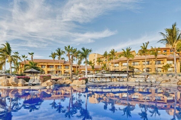 Relax by the pool surrounded by palm trees and hotel buildings.