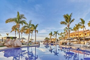 Relax by the resort pool surrounded by palm trees and lounge chairs, with umbrellas providing shade.