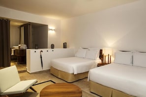 A hotel room with two beds, a sitting area, a small table, and a bathroom visible through an open door.