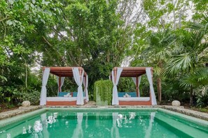 Un área de piscina con dos camas con dosel rodeadas de exuberante vegetación.