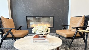 A modern living room with a round marble coffee table, two leather armchairs, a fireplace, and a decorative bowl with flowers. - The Heights Cozy Stay - Gym&pool 12mins to Midtown and Downtown (Houston)