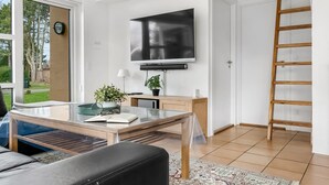A modern living room with a large TV, wooden furniture, a view through a glass door, and a patterned rug.