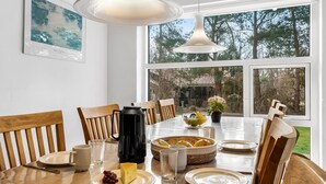 A dining area with a wooden table, chairs, and a view of the outdoors through large windows.
