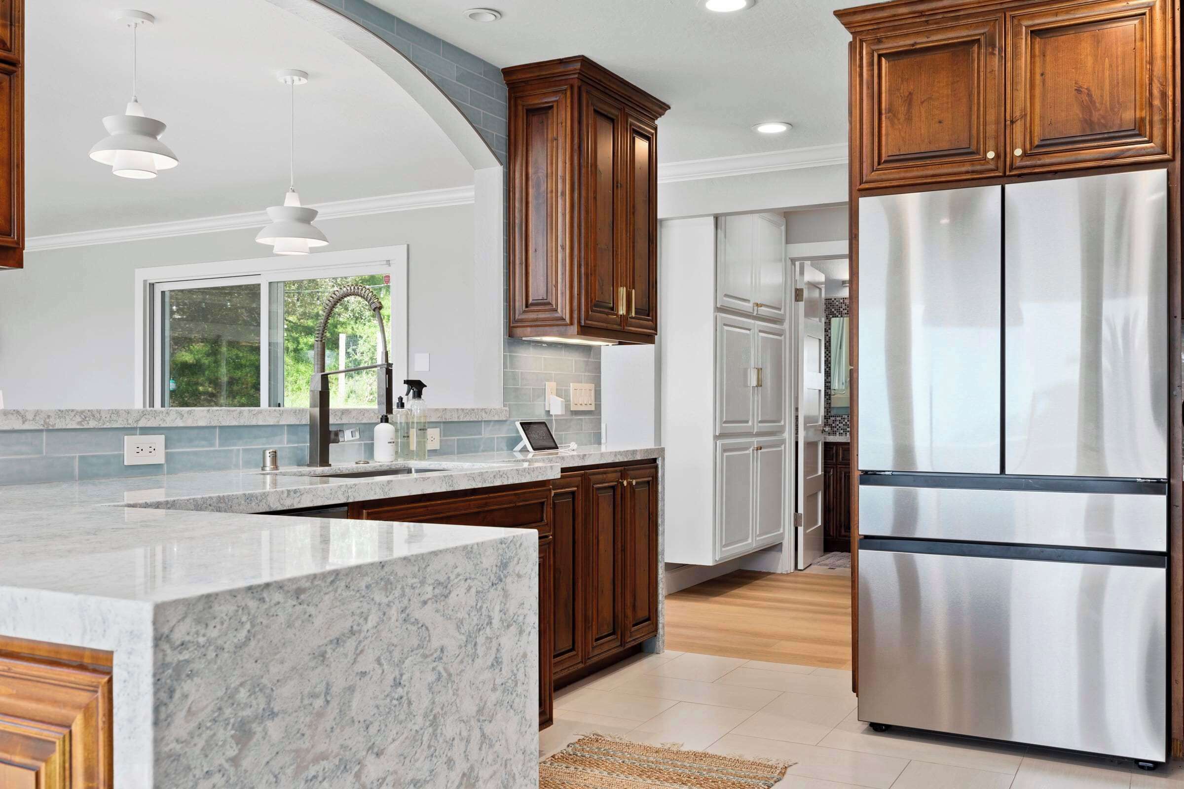 A modern kitchen with marble countertops, wooden cabinets, stainless steel appliances, and pendant lighting.