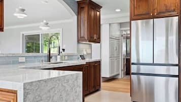 A modern kitchen with marble countertops, wooden cabinets, stainless steel appliances, and pendant lighting.